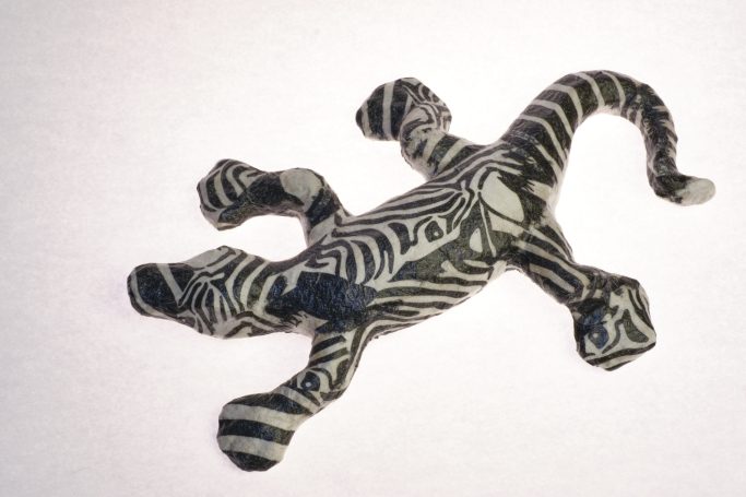 Ein gestreifter Gecko aus Pappmachee in Schwarz-weißem Zebramuster.